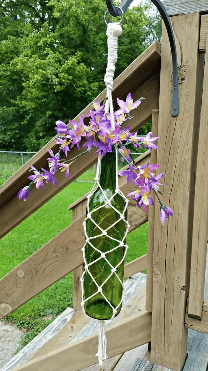 Wine bottle with purple flowers in it in a macrame holder