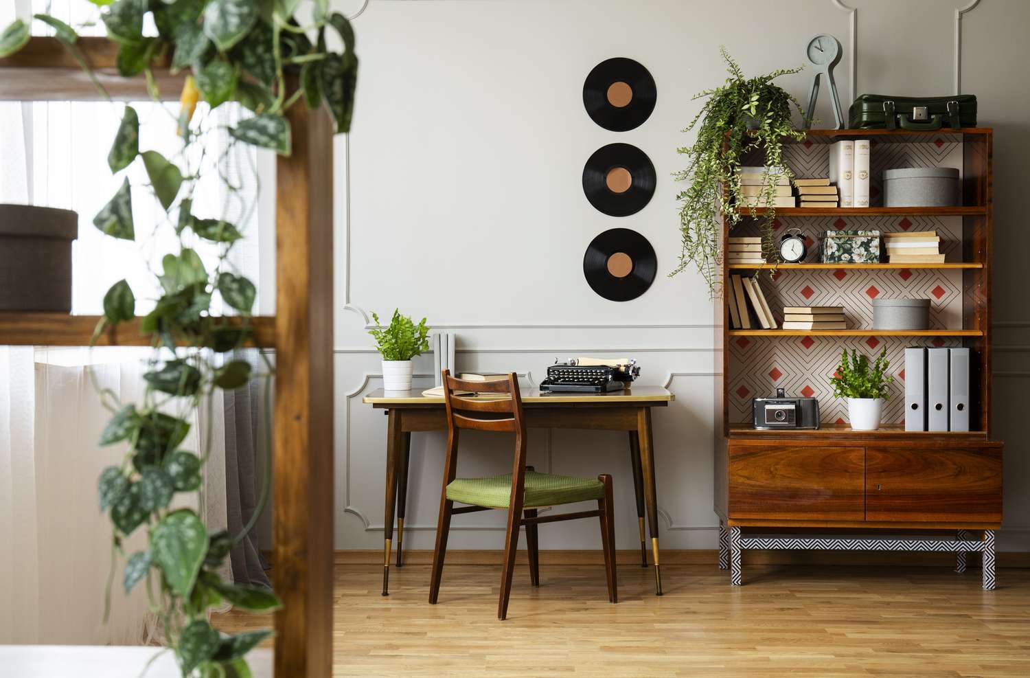 Svart retroskrivmaskin på ett unikt skrivbord i trä, en modern stol från mitten av århundradet och en renoverad bokhylla i en hipsterinredning för hemmakontor.