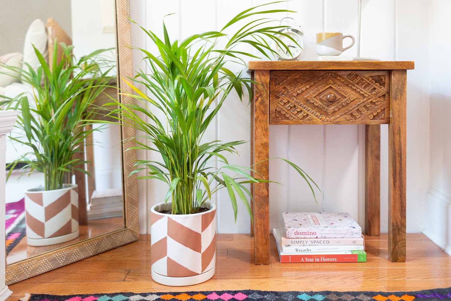 Areca-palm i vit och brunmönstrad kruka bredvid spegel och sidobord i trä