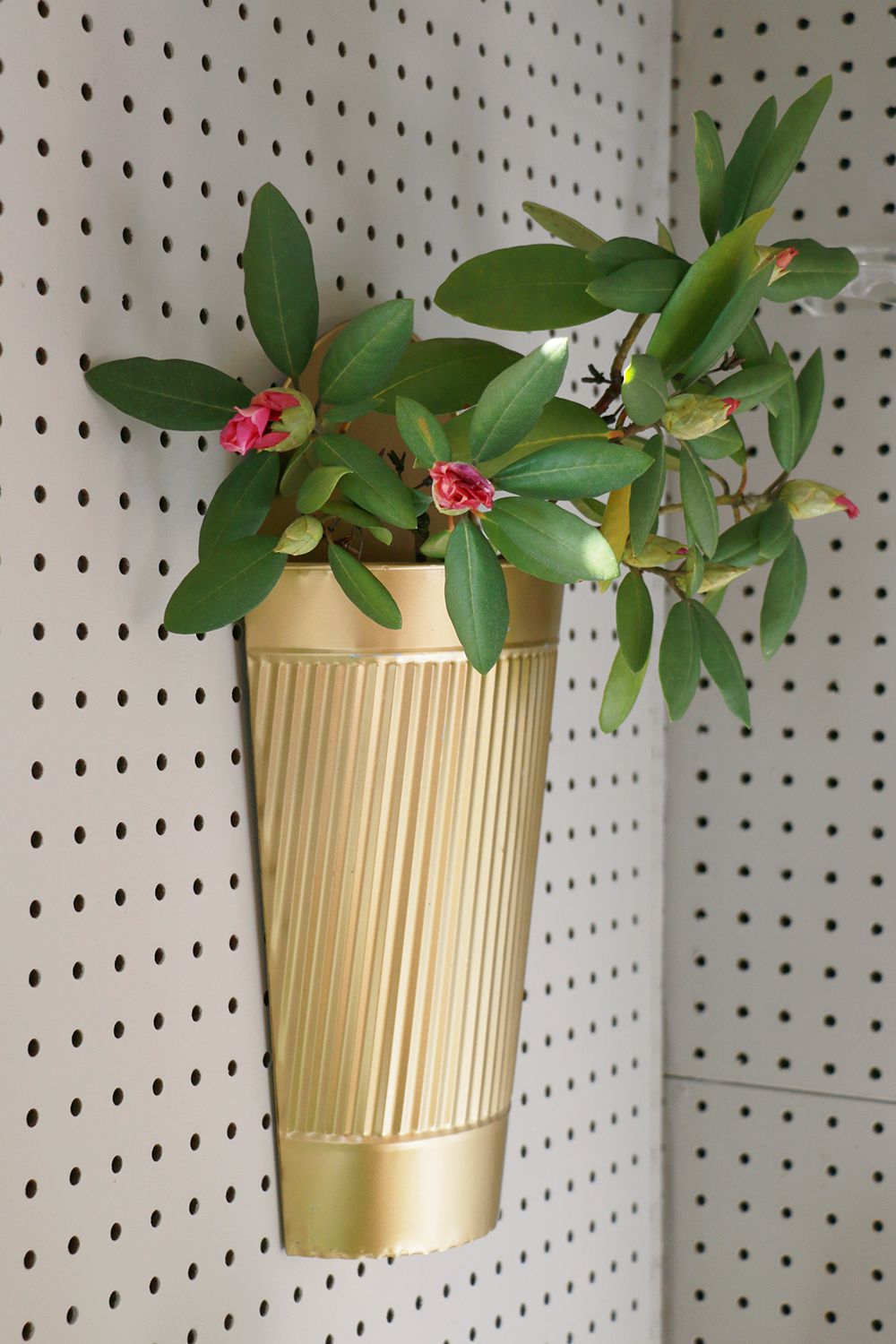 Blomkruka med blommor fäst på en pegboardvägg i ett skjul