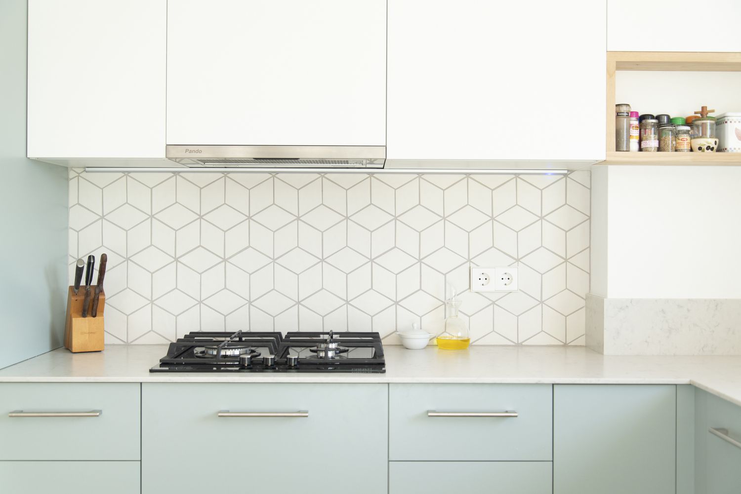 Litet kök med vita överskåp och mintgröna underskåp, samt geometriskt backsplash.