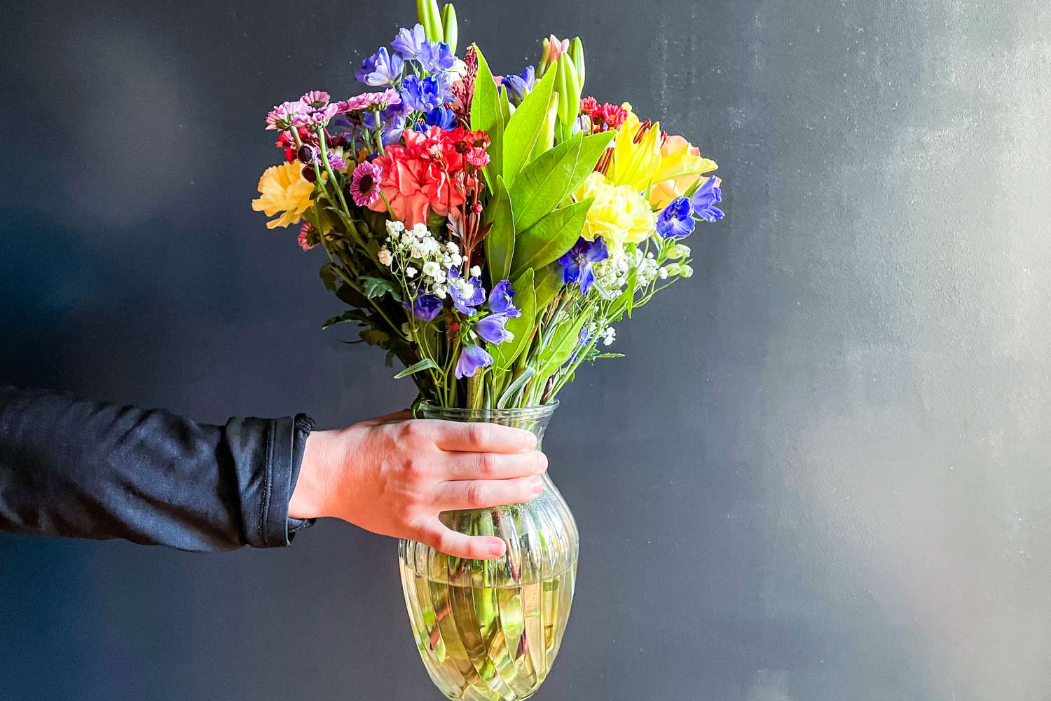 En hand som håller i en vas fylld med blommor från 1-800-Flowers