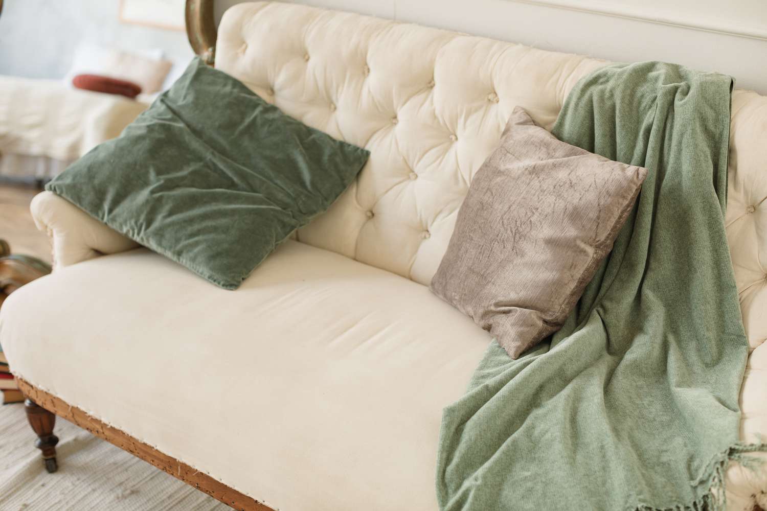 White tufted sofa with green and gray pillows and blanket