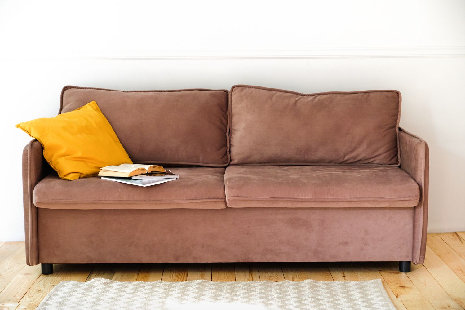 Brown suede couch with a yellow pillow