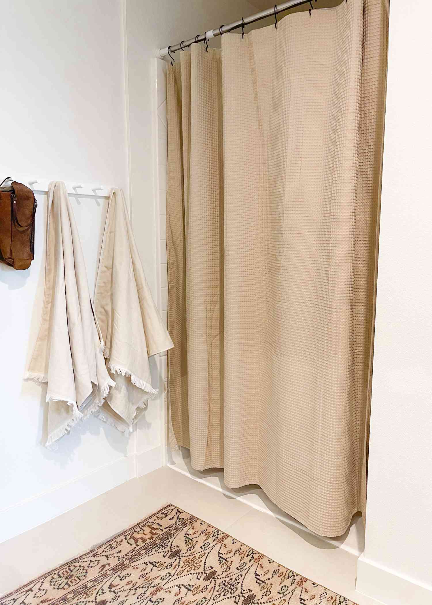 Ett beige duschdraperi används i ett vitt badrum