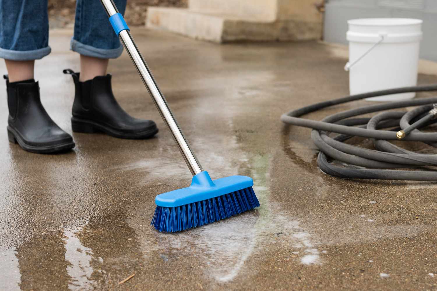 Kvast med nylonborste skrubbar rengöringslösning på obehandlad betongterrass