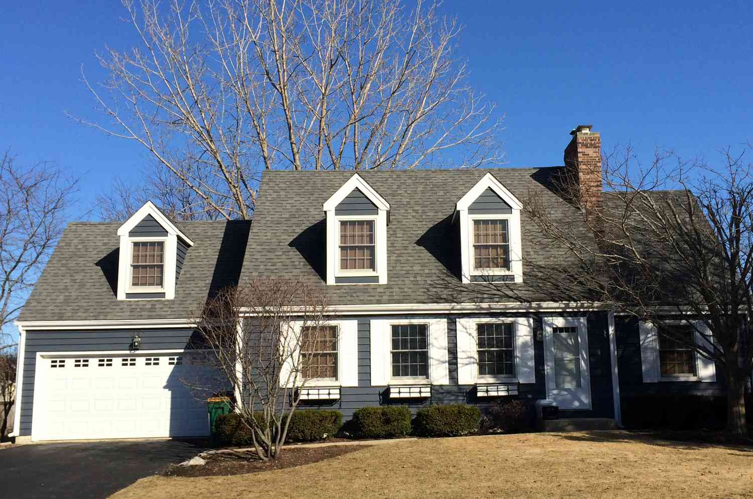 Hus i Cape Cod-stil med två takkupor på huset och en över garageporten.