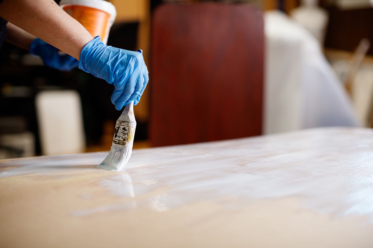 Hand in glove painting wooden board laying flat, using paintbrush and white paint