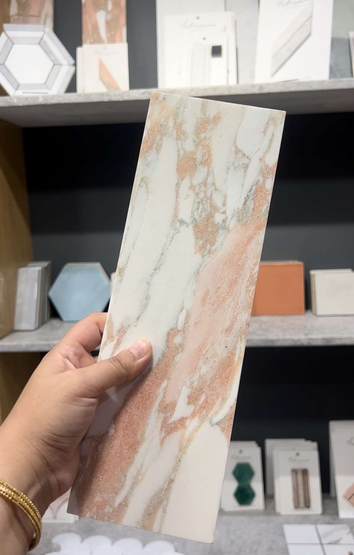 En bit kakel i rosa marmor i en butik med hyllor med kakelprover i olika former och storlekar