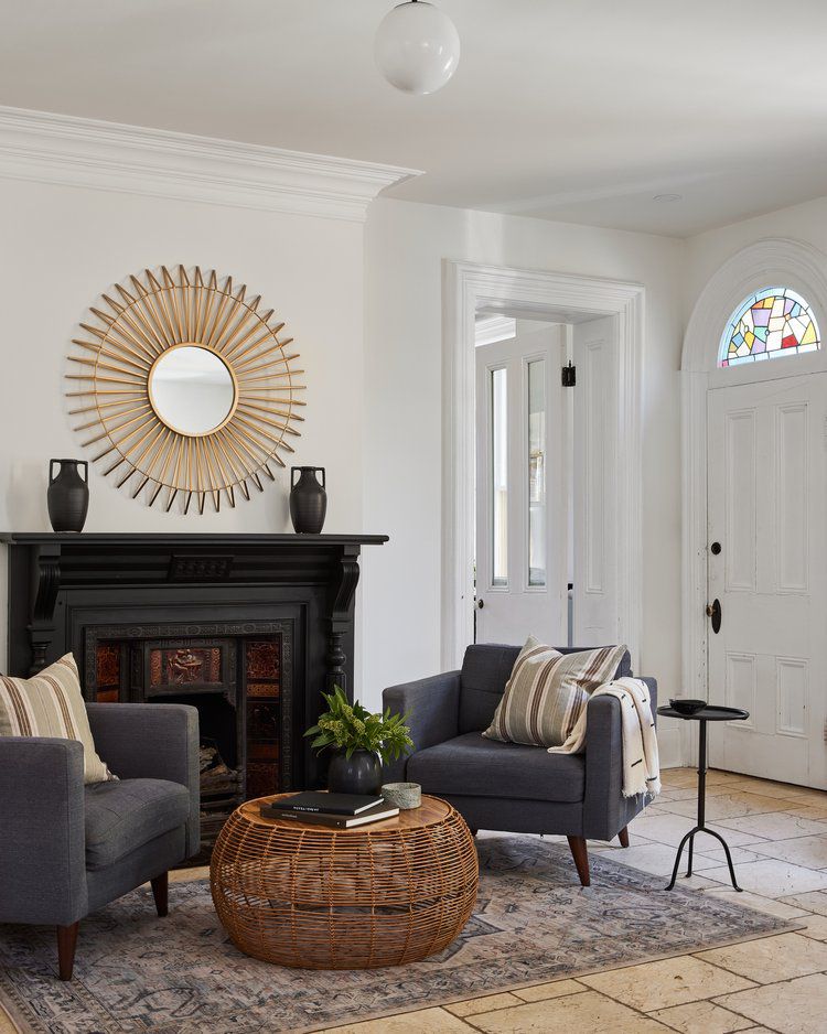 Eclectic historic modern living room with black fireplace facade, navy blue armchairs, and modern brass sunburst morrpr